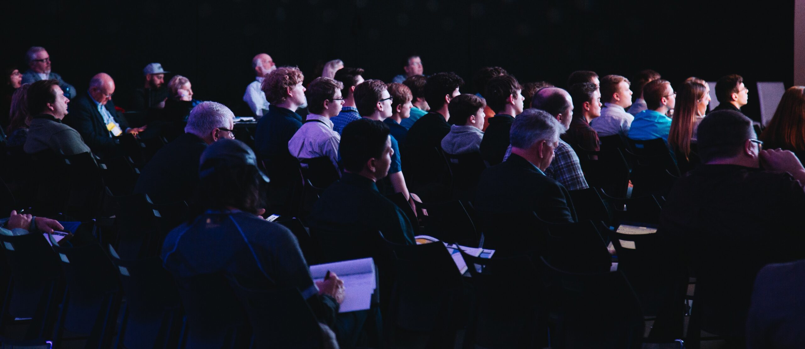 An audience of people sitting in a darkened auditorium at a conference